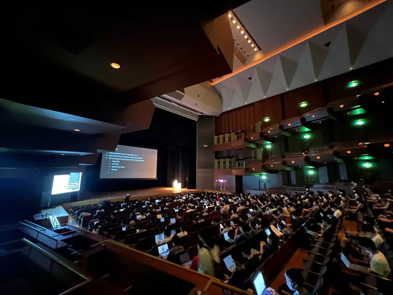 The RubyKaigi stage and many RubyKaigi attendees sitting in a large hall, many with laptops